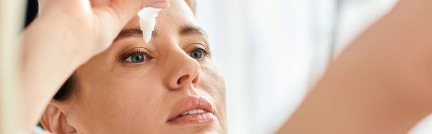 attractive blonde woman with collected hair in bathrobe putting in eye drops in her bathroom, banner - Photo, Image