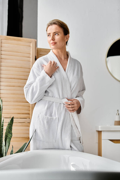красивая, весёлая женщина с светлыми волосами в белом удобном халате, позирующая рядом с ванной - Фото, изображение