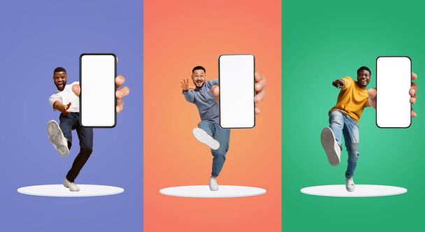 Αστεία πολυεθνική παιδιά που δείχνουν Big Blank Smartphones Στην κάμερα, ενώ στέκεται στην πλατφόρμα πάνω από πολύχρωμο Studio Backgrounds, Χαρούμενα Άνδρες Προτείνοντας νέα Mobile App, Κολάζ, Mockup - Φωτογραφία, εικόνα
