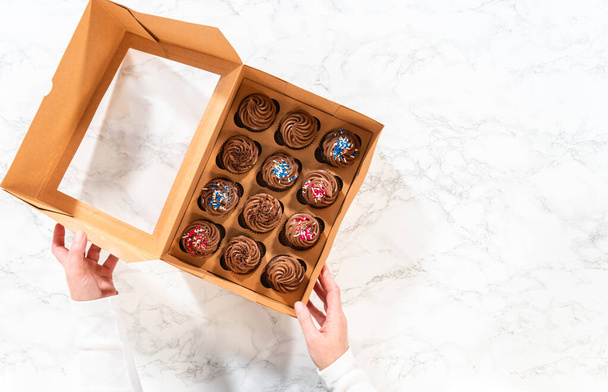 Flat lay. Preparing to share the delicious chocolate cupcakes, the final step involves carefully packaging them into a brown paper cupcake box. - Photo, Image