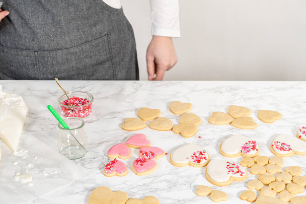 Dekorowanie ciasteczek w kształcie serca z różowym i białym królewskim lukrem na Walentynki. - Zdjęcie, obraz