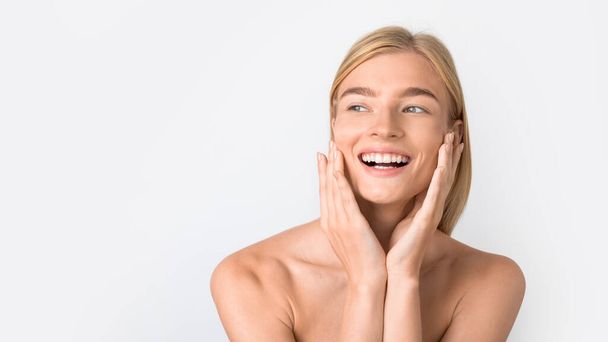 Attractive happy caucasian lady touching her face, highlighting routine of facial skincare and natural beauty, posing with bare shoulders against pure white studio backdrop. Panorama, copy space - Photo, Image