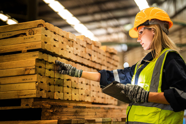 női munkás ács visel biztonsági egyenruhát és kemény kalapot dolgozik, és ellenőrzi a minőség a fából készült termékek műhelyben gyártás. férfi és nő munkások fa sötét raktár ipar. - Fotó, kép