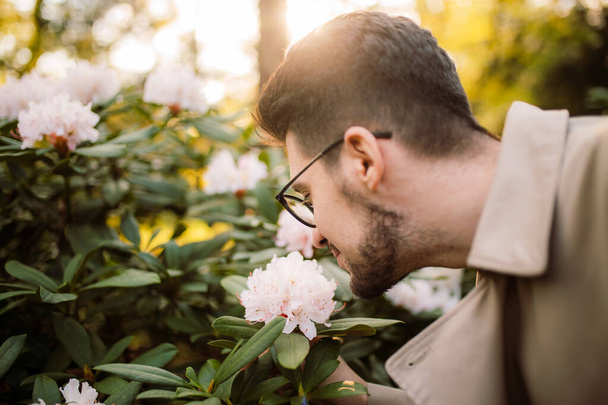 Un giovane uomo elegante odora fiori primaverili nel parco al tramonto in una giornata di sole. E 'primavera. Relax, gioventù, stile di vita solitudine con la natura - Foto, immagini