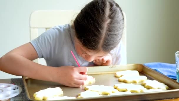 Une scène chaleureuse d'une petite fille écrivant avec soin Désolé sur les biscuits au sucre avec colorant alimentaire, les biscuits magnifiquement inondés de glaçage royal blanc. - Séquence, vidéo