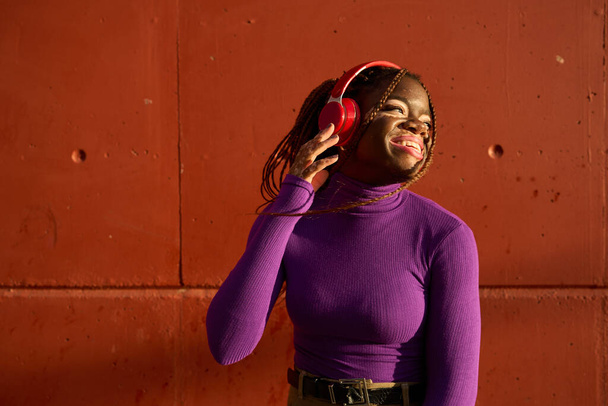Жінка з вітіліго насолоджується музикою з червоними навушниками, міський фон стіни. - Фото, зображення