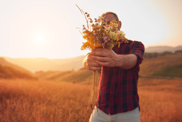 Hombre recogiendo y sosteniendo flores de campo en la naturaleza. - Foto, imagen