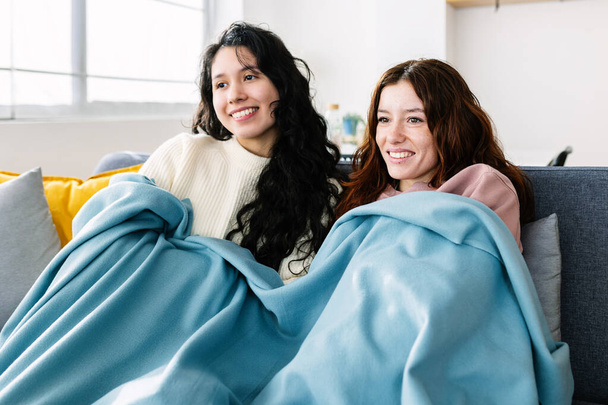 Glückliche junge Millennials, die es sich mit einer Decke zugedeckt auf dem Sofa gemütlich machen und im Winter gemeinsam fernsehen - Foto, Bild