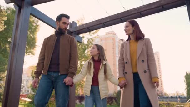 Boldog kaukázusi család anya apa gyermek lány lánya gyerek séta együtt séta a parkban kéz a kézben beszél beszél beszélgetés boldogság gyermekkor a városban hétvégén kívül egészségbiztosítás - Felvétel, videó