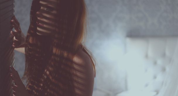 Silhouet vrouw op zoek via jaloezieën - Foto, afbeelding