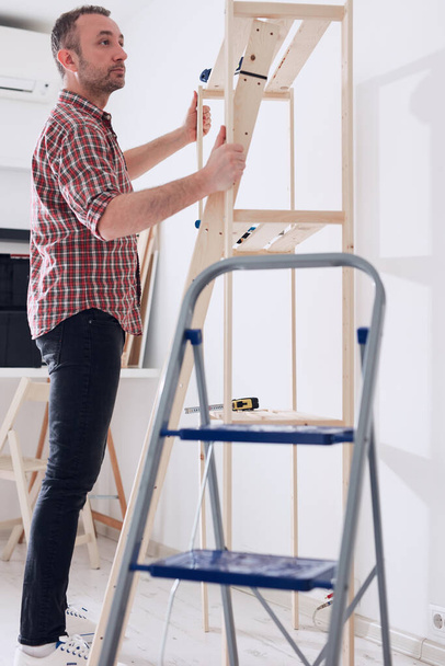 Άνδρας συναρμολόγηση νέων ξύλινων ραφιών και επίπλων στο διαμέρισμα. - Φωτογραφία, εικόνα