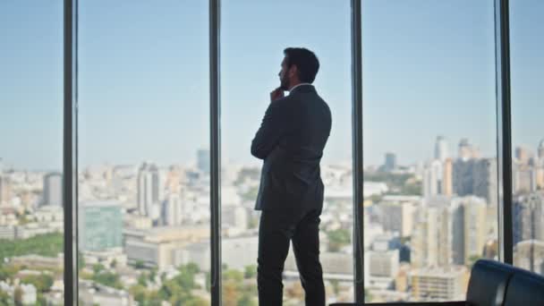 Στοχαστικός άντρας που δείχνει πανοραμικό παράθυρο στο γραφείο. Νομική διευθυντής εξετάζει πόλη κτίρια σχεδιασμό της στρατηγικής της εταιρείας στο χώρο εργασίας οπίσθια όψη. Μη αναγνωρισμένη σιλουέτα λήψης επιχειρηματικών αποφάσεων. - Πλάνα, βίντεο