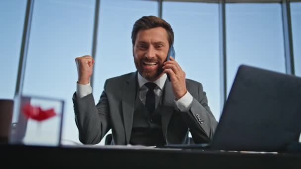Onnellinen yrittäjä nauttii puhelun liiketoiminnan voitto toimistossa lähikuva. Innoissaan mies Executive Check asiakirjat saada hyviä uutisia älypuhelin keskustelu. Iloinen myyntipäällikkö keskustelee onnistuneesta kaupasta - Materiaali, video
