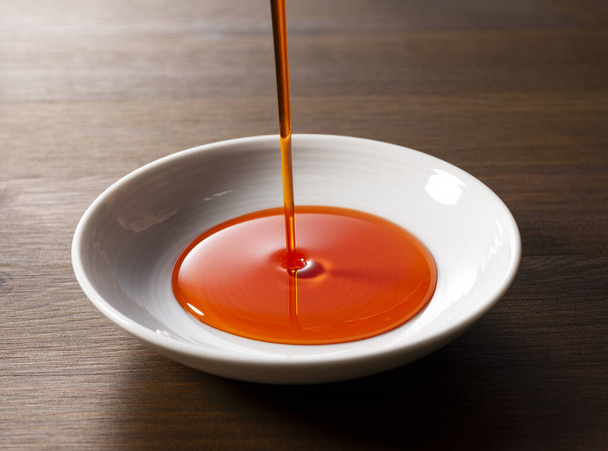 Verser la sauce à l'huile de chili dans un plat en céramique. Fond en bois. Tableau. - Photo, image