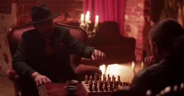 Dospělý muž v obleku a čepice sedí na křesle hraje šachovnici hru s anonymní přítel doma v noci - Záběry, video
