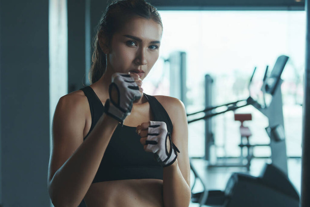 Donna sportiva che indossa guanti da boxe posa in posizione di combattimento guardando la fotocamera. - Foto, immagini