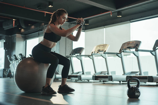Sportowa kobieta robi trening i za pomocą fitball siedząc i balansując na nim. - Zdjęcie, obraz