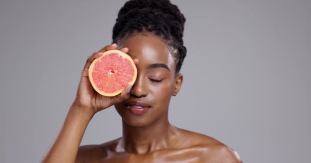 Grapefruit, beauty and woman in studio for healthy glow, vitamin c benefits or collagen on grey background. African model, citrus fruits and dermatology for skincare, eco cosmetics or detox nutrition. - Footage, Video