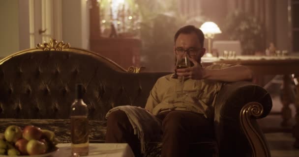 Προσεκτική ενήλικη γενειοφόρος αρσενικό αρωματοποιός προσπαθεί να δημιουργήσει άρωμα, ενώ πίνοντας κρασί κάθεται σε vintage καναπέ στο σπίτι - Πλάνα, βίντεο