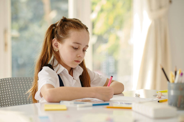 Kreatív iskoláslány rajz tankönyvbe az iskola asztalánál - Fotó, kép