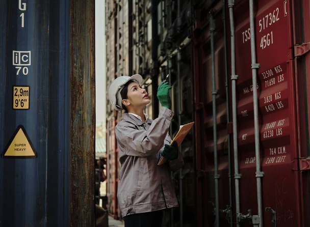 Portrait d'une travailleuse tenant un presse-papiers debout devant un conteneur d'entrepôt . - Photo, image