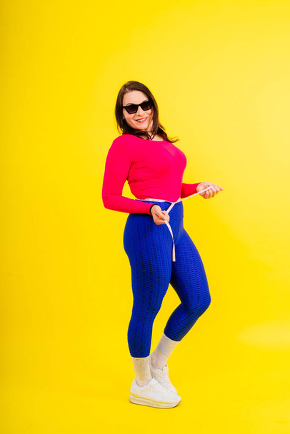 Bastante hembra con exceso de peso en una parte superior deportiva que mide la cintura sobre fondo amarillo blanco - Foto, Imagen