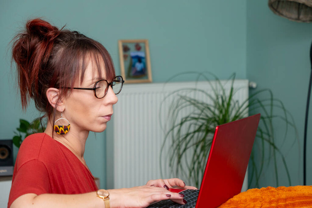 Ciddi bir genç kadın evde dizüstü bilgisayar kullanıyor. - Fotoğraf, Görsel