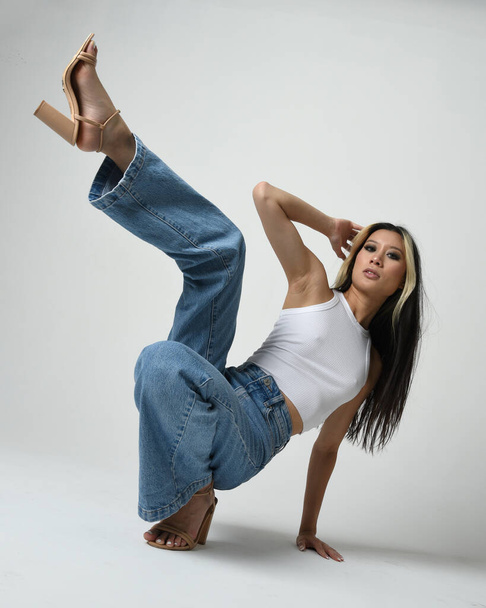 Портрет брюнетки жіночої азіатської моделі в повсякденному одязі, біла сорочка-синглет, джинсові штани. Зручна сидяча поза. Ізольовані на білому фоні студії. - Фото, зображення
