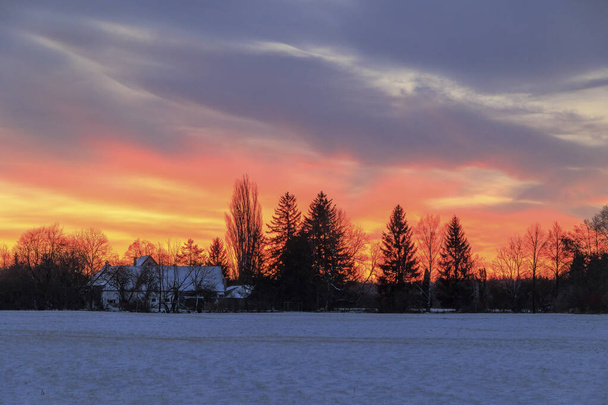 Bunter Sonnenaufgang mit leuchtend roten Wolken an einem Wintertag über den Wiesen und Wäldern von Siebenbrunn, dem kleinsten Stadtteil der Fuggerstadt Augsburg - Foto, Bild