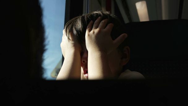 Uitgeput Kind wrijven Ogen op Moving Train, Wakker worden uit Nap door raam tijdens het reizen, zichzelf te beschermen tegen zonnestralen - Foto, afbeelding