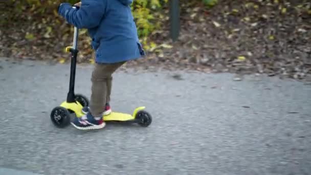 Kapalı çocuk ayakları dışarıda üç tekerlekli scooter sürüyor. - Video, Çekim