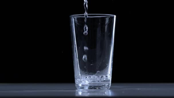 Agua potable limpia se vierte en un vaso de vidrio sobre un fondo negro - Metraje, vídeo