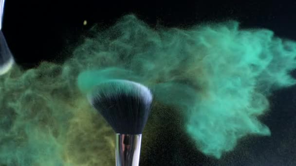 Grünes und gelbes Kosmetikpuder kollidieren in Superzeitlupe mit Kosmetikbürsten und in der Luft fliegenden Partikeln - Filmmaterial, Video