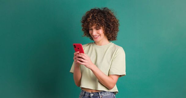 Smiling young female with mobile phone on green background - Photo, Image