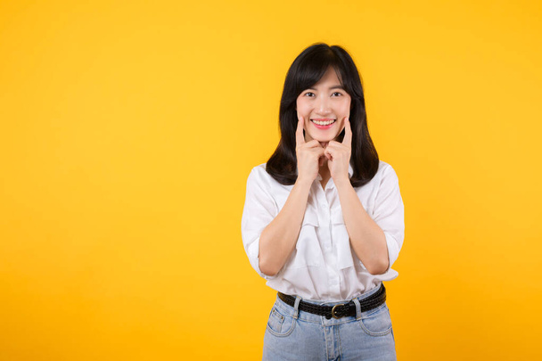 Jonge Aziatische mooie vrouw vrolijke glimlach dragen witte shirt en spijkerbroek jean planten over geel geïsoleerde achtergrond glimlachen zelfverzekerd tonen en wijzen met vingers tanden en mond. Tandheelkundig concept. - Foto, afbeelding