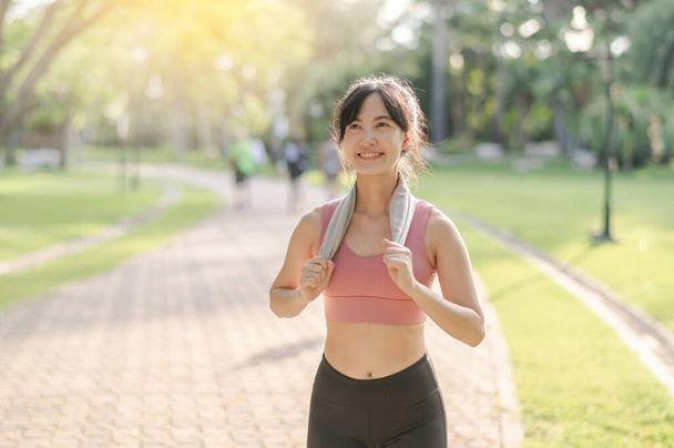 Fit sonrisa feliz 30s joven mujer asiática en ropa deportiva disfruta de refrescante puesta de sol correr en la naturaleza. La silueta de la figura contra el sol poniente es hermosa vista. Concepto de aptitud, salud o motivación. - Foto, imagen