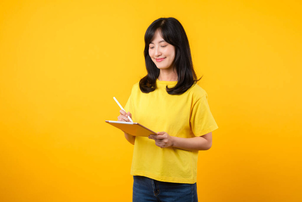Experience the joy of education technology with portrait. A Asian young woman wearing a yellow t-shirt and denim jeans showcases a happy smile while using digital tablet. education technology concept. - Photo, Image