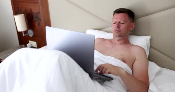 Figyelmes koncentrált férfi dolgozik laptop feküdt az ágyban. Távmunka és a szabadúszó élete - Felvétel, videó