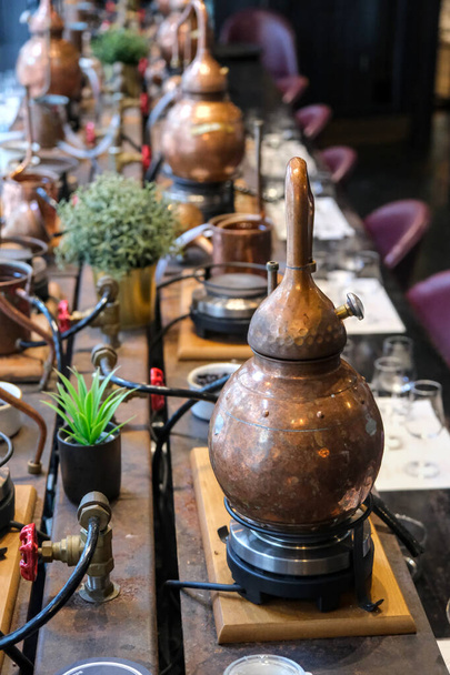 Pequeños alambiques de cobre y equipo de destilación dispuestos en una mesa decorada. - Foto, imagen