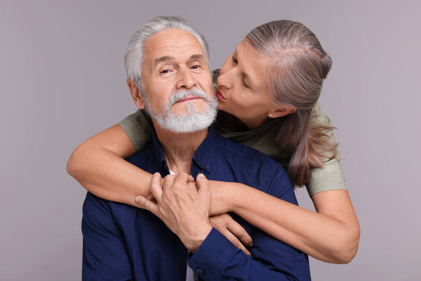 Senior woman kissing her beloved man on light grey background - Фото, зображення