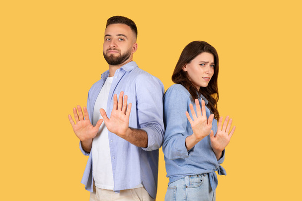 ジェスチャーを止めるために前方に手のひらを示す男性と女性, 慎重な表現や拒否を示唆しています, きれいな黄色の背景に対して, - 写真・画像