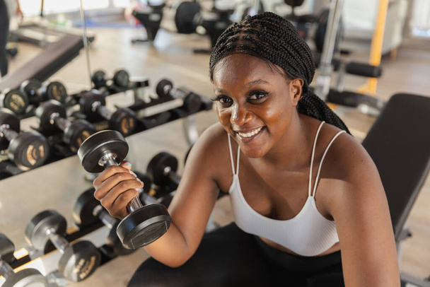 健康な強い女性アフリカ系アメリカ人プラスサイズのホールディングダンベルは,ジムで体重運動を持ち上げます. スポーツトレーニングウェイトフィットネス,体重を減らすための運動,健康の世話. - 写真・画像