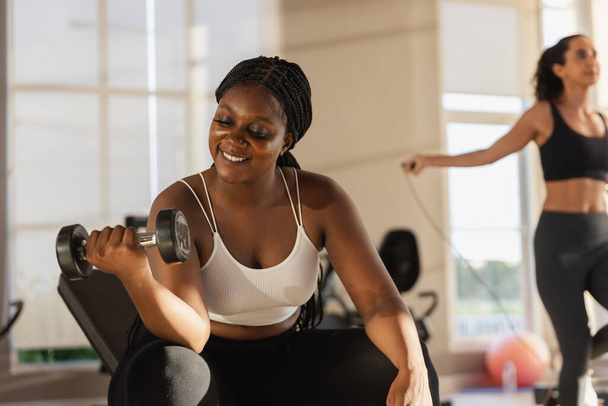 Sağlıklı, güçlü, Afrikalı, büyük boy halterli kadın spor salonunda ağırlık kaldırıyor. Spor antrenmanları ağırlık azaltma egzersizleri, kilo verme egzersizleri, sağlık hizmetleri.. - Fotoğraf, Görsel