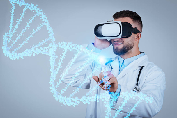 Expert mladý lékař ve VR sluchátkách zkoumá vibrující virtuální DNA vlákno s přesností CRISPR, postupující péči o pacienta prostřednictvím rozšířené reality, modré pozadí studia - Fotografie, Obrázek