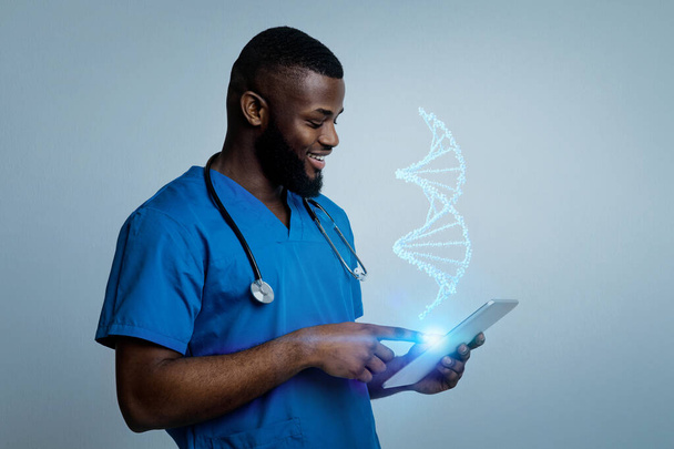 Progrès des diagnostics santé. Professionnel jeune homme noir médecin étudiant brin d'ADN virtuel sur tablette numérique, fond studio bleu - Photo, image