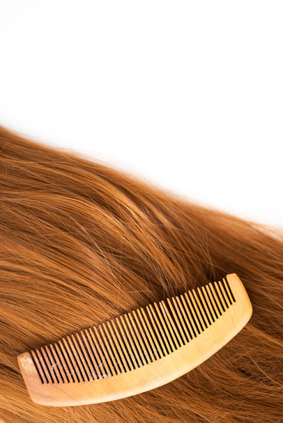 Um pente de madeira em um marrom longas extensões sintéticas brilhantes de peruca cabelo marrom sintético - Foto, Imagem
