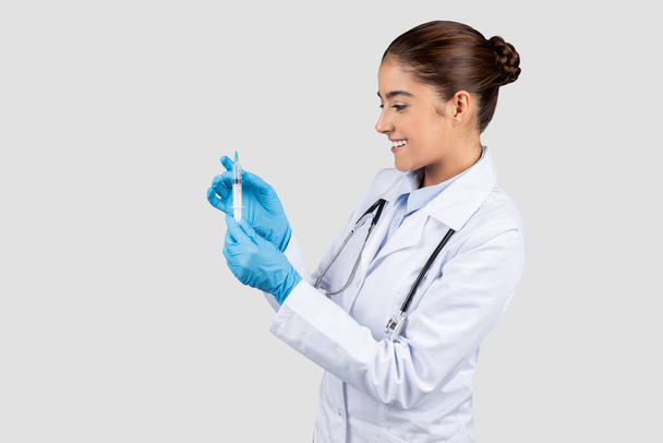 Dama branca milenar alegre doutor no casaco branco mostra a seringa com a vacina no fundo claro. Injeção de gripe, cuidados de saúde, terapia e recomendação de vacinação - Foto, Imagem