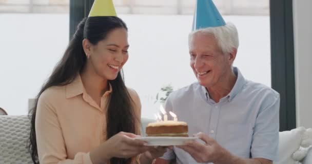 Blowing out candles, old man and girl with birthday, face and celebration with happiness, retirement and relax. Party hats, cake and excited with joy, pensioner and friend on a couch, love and home. - Footage, Video