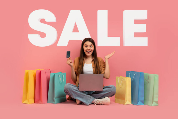 Большие продажи. Возбужденные девочка-подросток покупки в Интернете с ноутбуком и кредитной картой сидит среди бумажных пакетов, делая покупки в Интернете, за розовым студио фон с Word SALE, коллаж - Фото, изображение