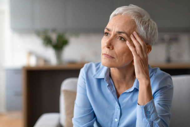 Ritratto di donna anziana europea infelice che tocca la testa sofferente di mal di testa, guardando da parte con espressione depressa, seduta sul divano in soggiorno a casa. Spazio libero per l'offerta - Foto, immagini